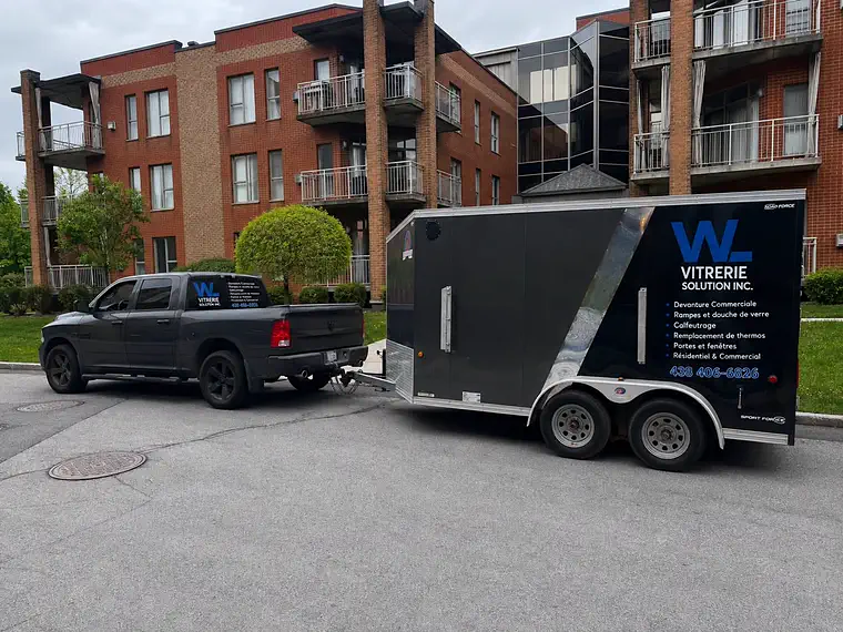 Camion et remorque aux couleurs de WL Vitrerie Solution stationnés devant un immeuble résidentiel.