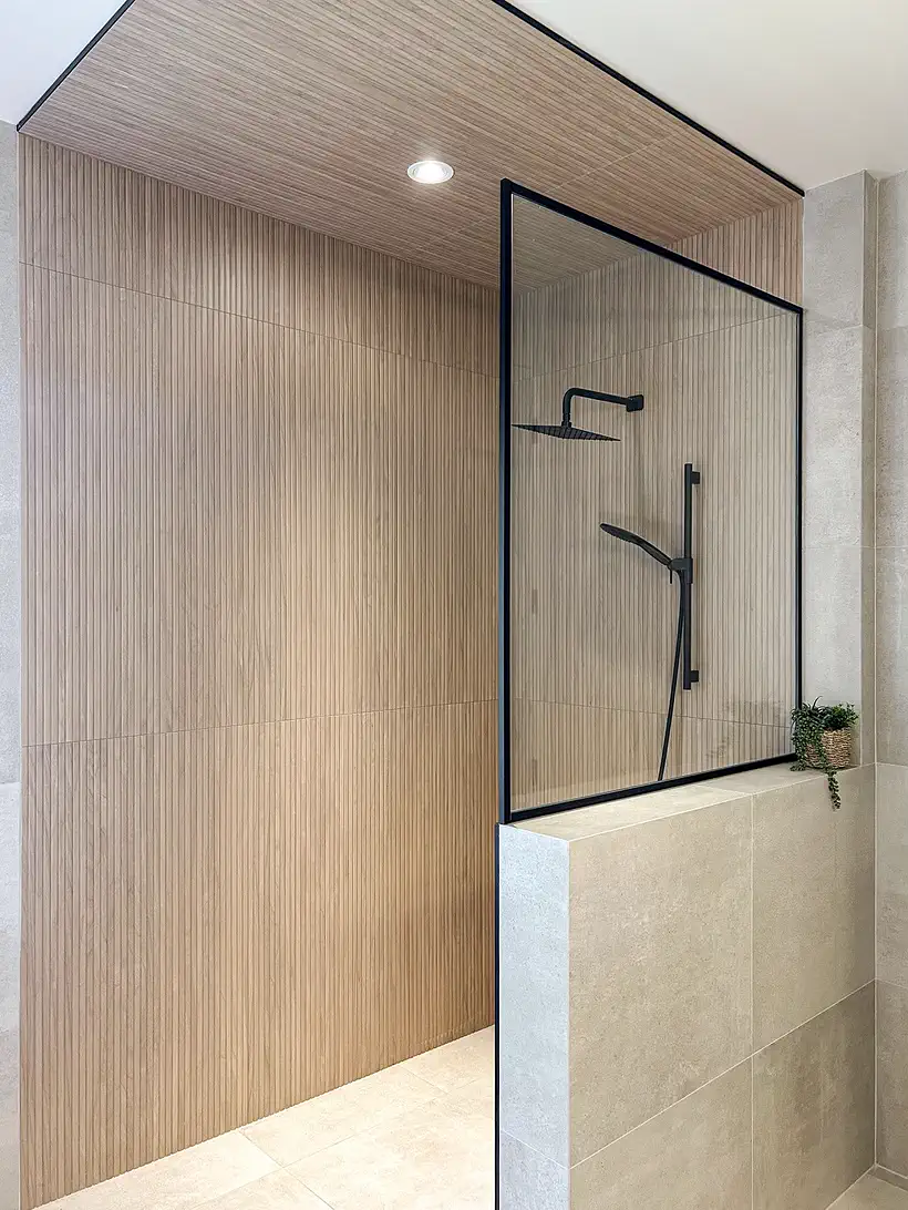 Douche à l'italienne avec panneau de verre à cadre noir, murs de tuile beige et plafond de bois.