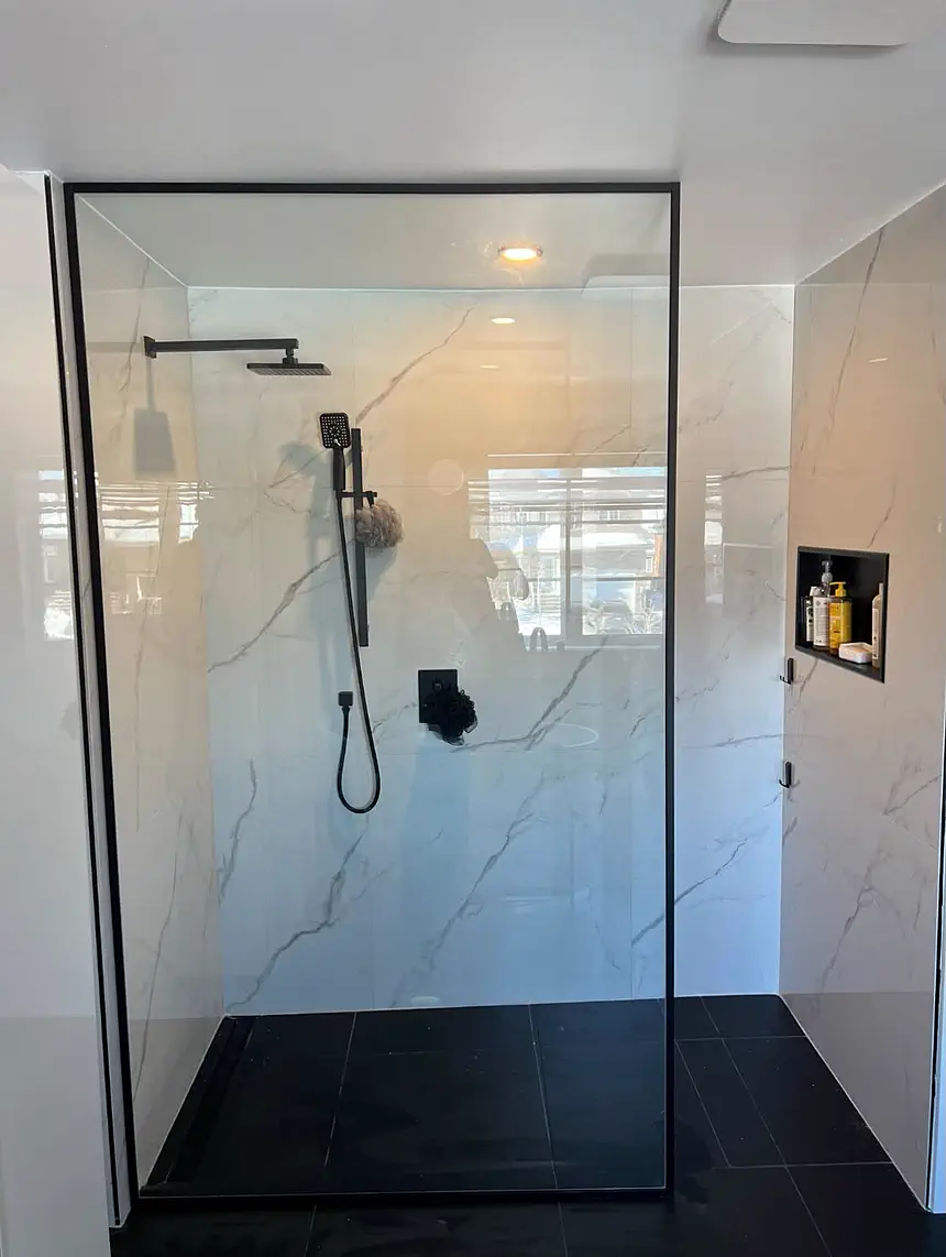 Douche à l'italienne : panneau de verre à cadre noir, mur de marbre blanc, base d'ardoise et niche encastrée.