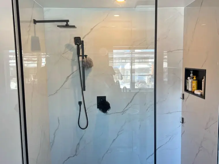 Douche en verre trempé avec cadre noir sur mur de marbre blanc.